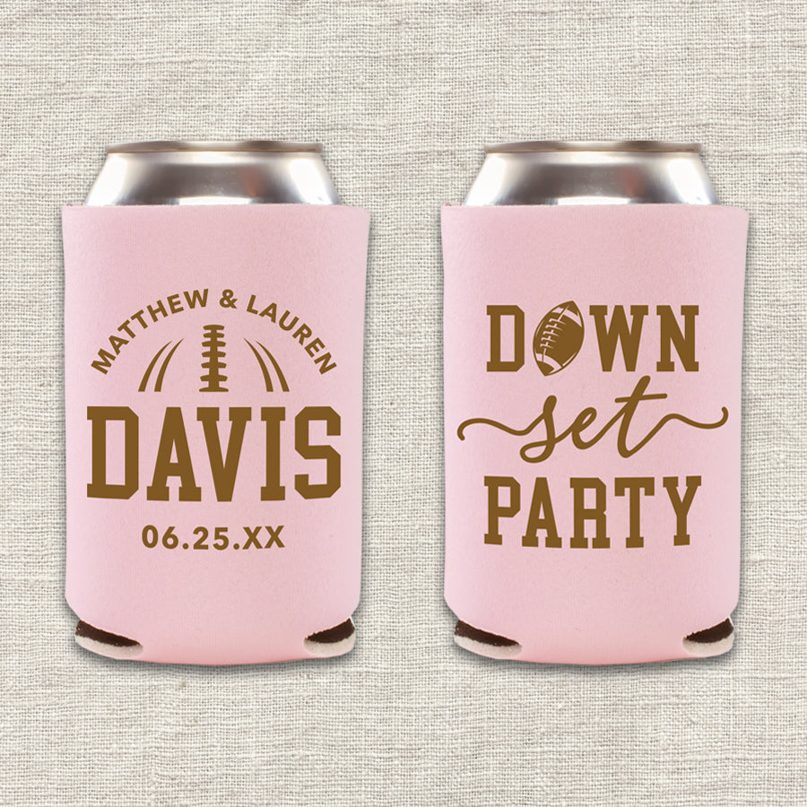 Two collapsible foam can coolers are shown on a beige background. The can coolers are blush pink, and the writing on them is brown. The can cooler on the left says the couple's first names, last name, and wedding date. The can cooler on the right says "Down, Set, Party" with an image of a football. 