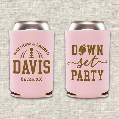 Two collapsible foam can coolers are shown on a beige background. The can coolers are blush pink, and the writing on them is brown. The can cooler on the left says the couple's first names, last name, and wedding date. The can cooler on the right says "Down, Set, Party" with an image of a football. 