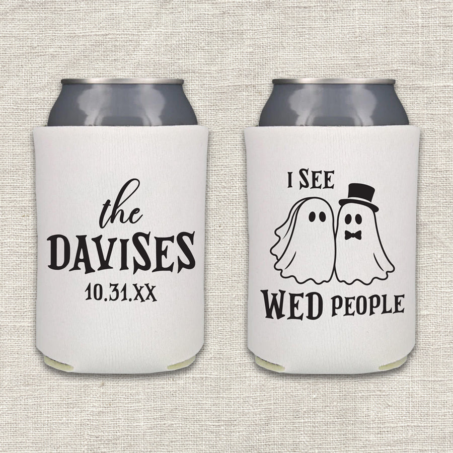 Two white can coolers are displayed side-by-side on a textured beige fabric background. The left cooler features the couple's last name and wedding date. The right can cooler features the words "I See WED People," along with bride and groom cartoon images.