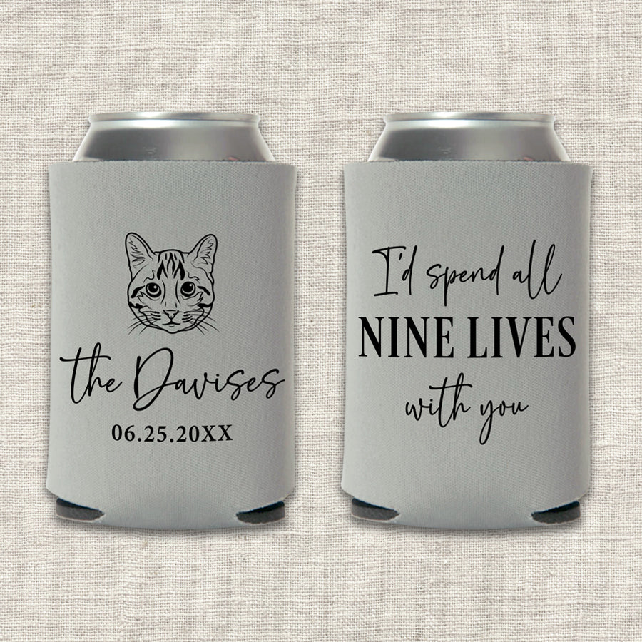 Two gray can coolers with a custom cat illustration and text that says "I'd spend all nine lives with you" on a textured beige background