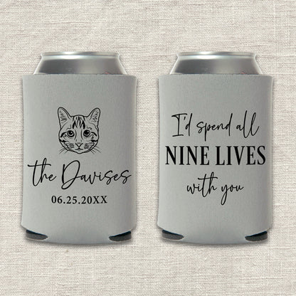Two gray can coolers with a custom cat illustration and text that says "I'd spend all nine lives with you" on a textured beige background