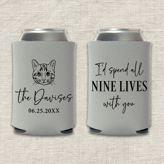 Two gray can coolers with a custom cat illustration and text that says "I'd spend all nine lives with you" on a textured beige background
