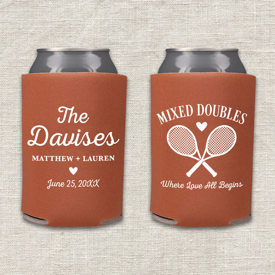Two rust-colored can coolers displayed side by side on a light beige textured fabric background. The left can cooler is personalized with 'The Davises', the names 'Matthew + Lauren', and a wedding date. The right can cooler features the text 'Mixed Doubles - Where Love All Begins.'