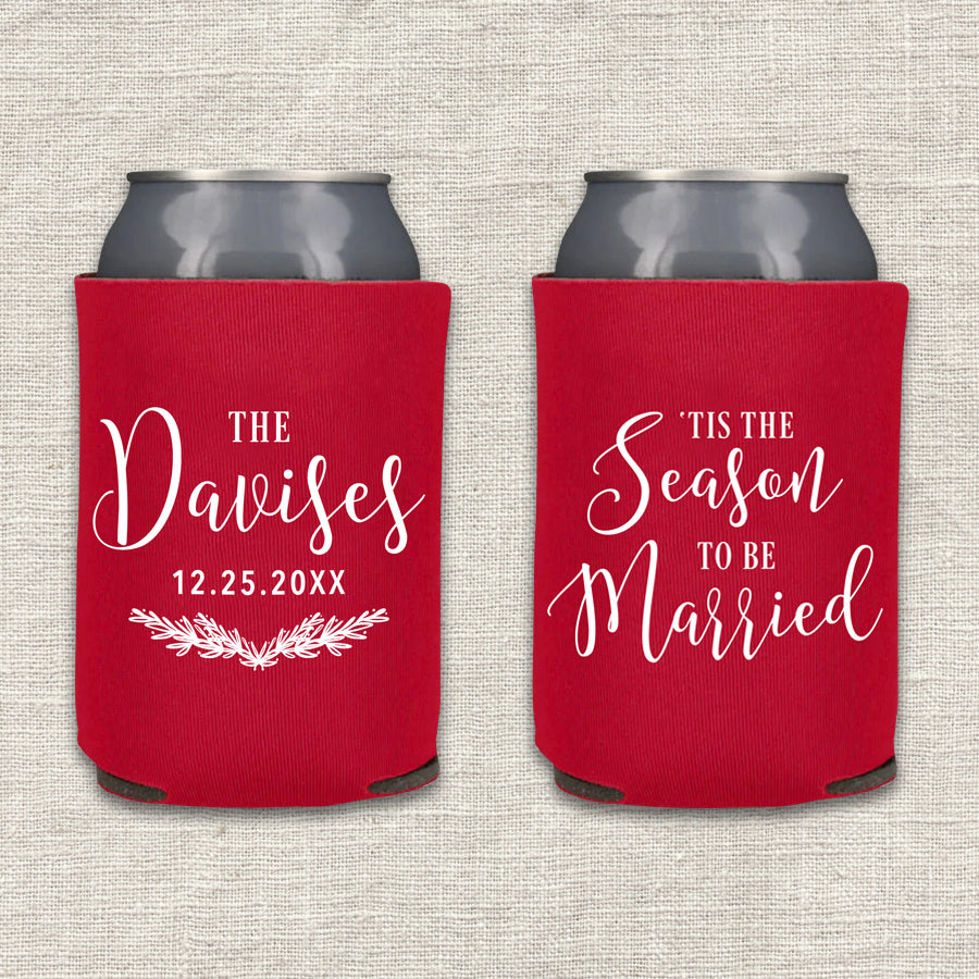 Two collapsible foam can coolers are shown on a textured beige background. The can coolers are red, and the writing on the can coolers is white. The can cooler on the left says the couple's last name and wedding date, along with a pine branch laurel. The can cooler on the right says "'Tis the Season to be Married."